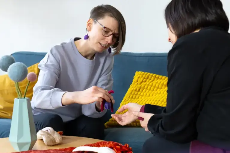 Ricarda Thiele sitzt auf ihrem Beratungssofa, sie unterhält sich mit einer Klientin. In der Hand hält sie einen Kunsstoff-Uterus.