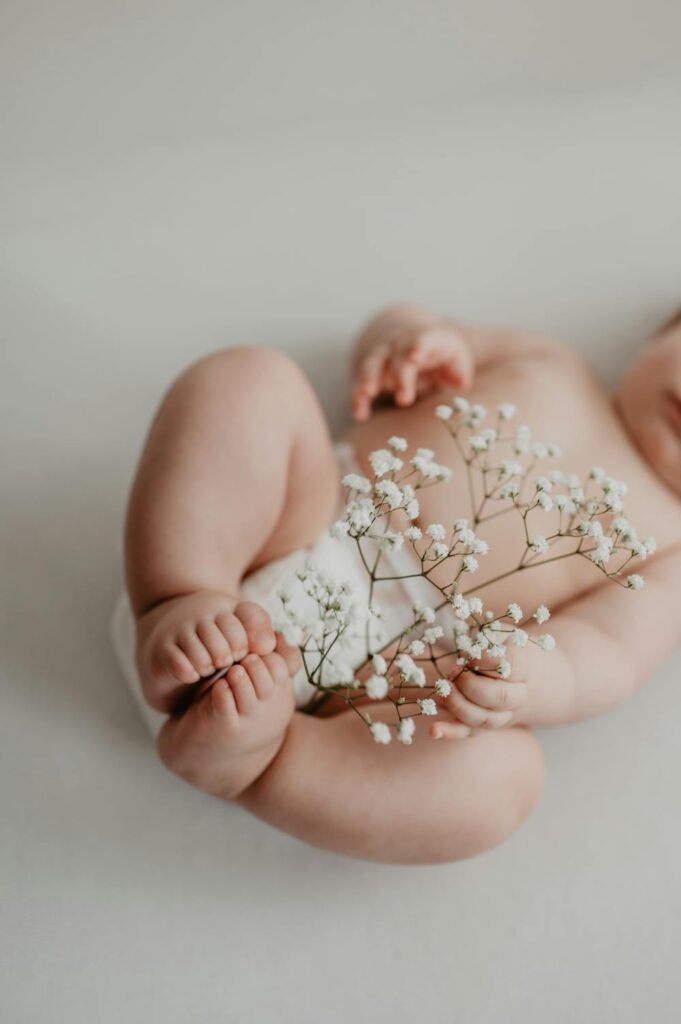 Ein Baby in Windel und einer Blume iin der Hand. Die kleinen knuffigen Beinchen sind in die Luft gestreckt.