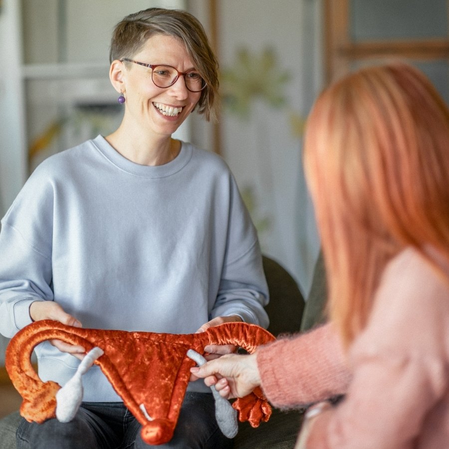 Ricarda Thiele berät eine Frau und hält dabei eine Stoff-Gebärmutter in Händen