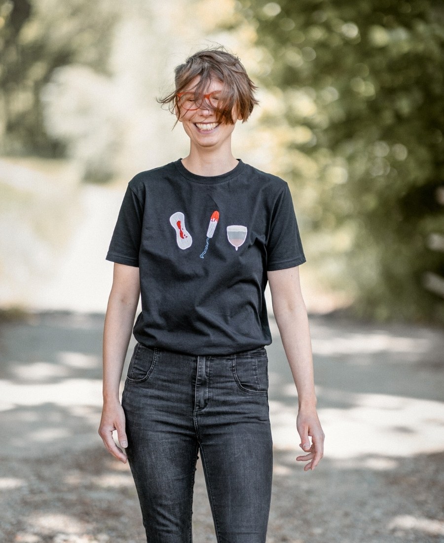 Ricarda Thiele lächelt herzlich. Sie hat ein lustiges Shirt an. Darauf sind Eine Binde, Ein Tampon und eine Menstruationstasse